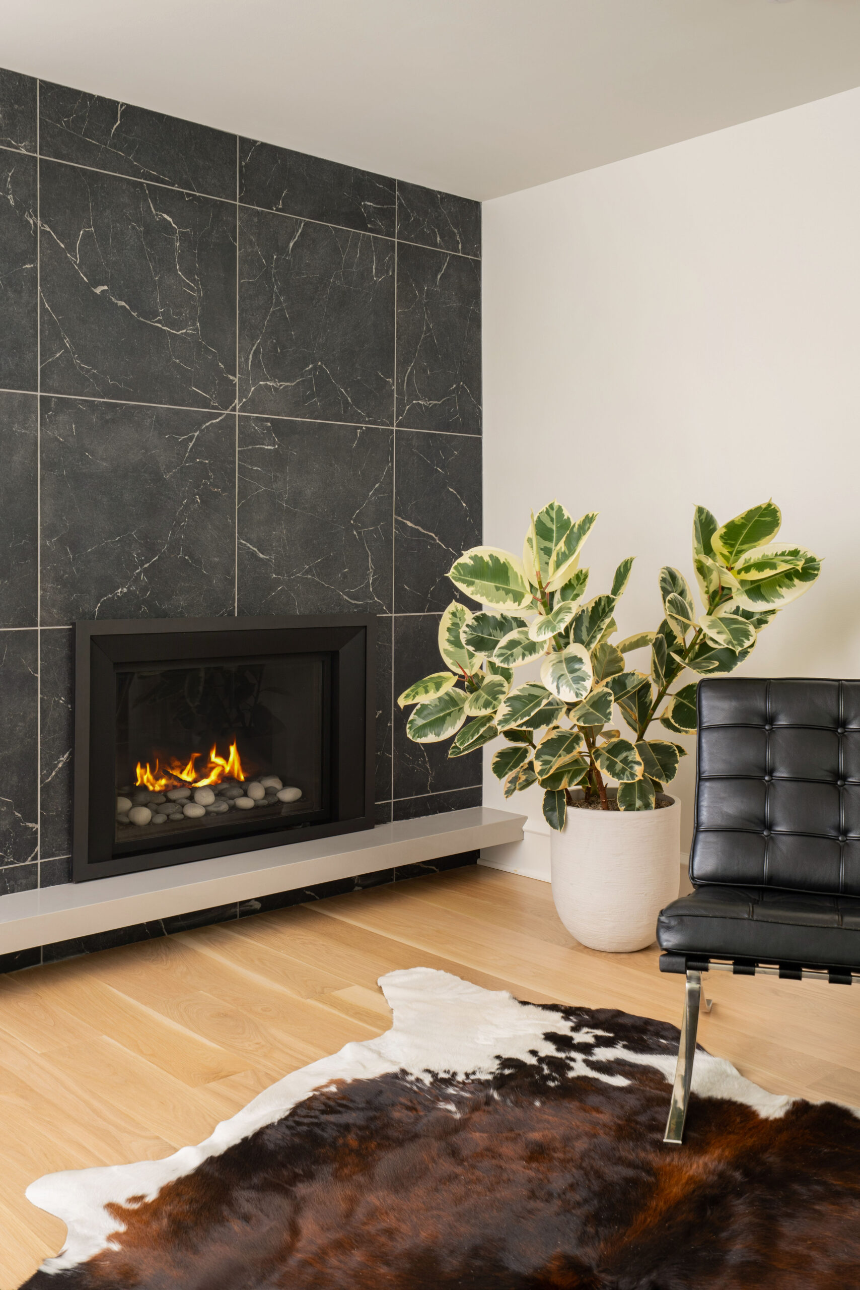 Modern parlor with new stone-surround fireplace, black marble tile wall, leather chair, and warm oak flooring.