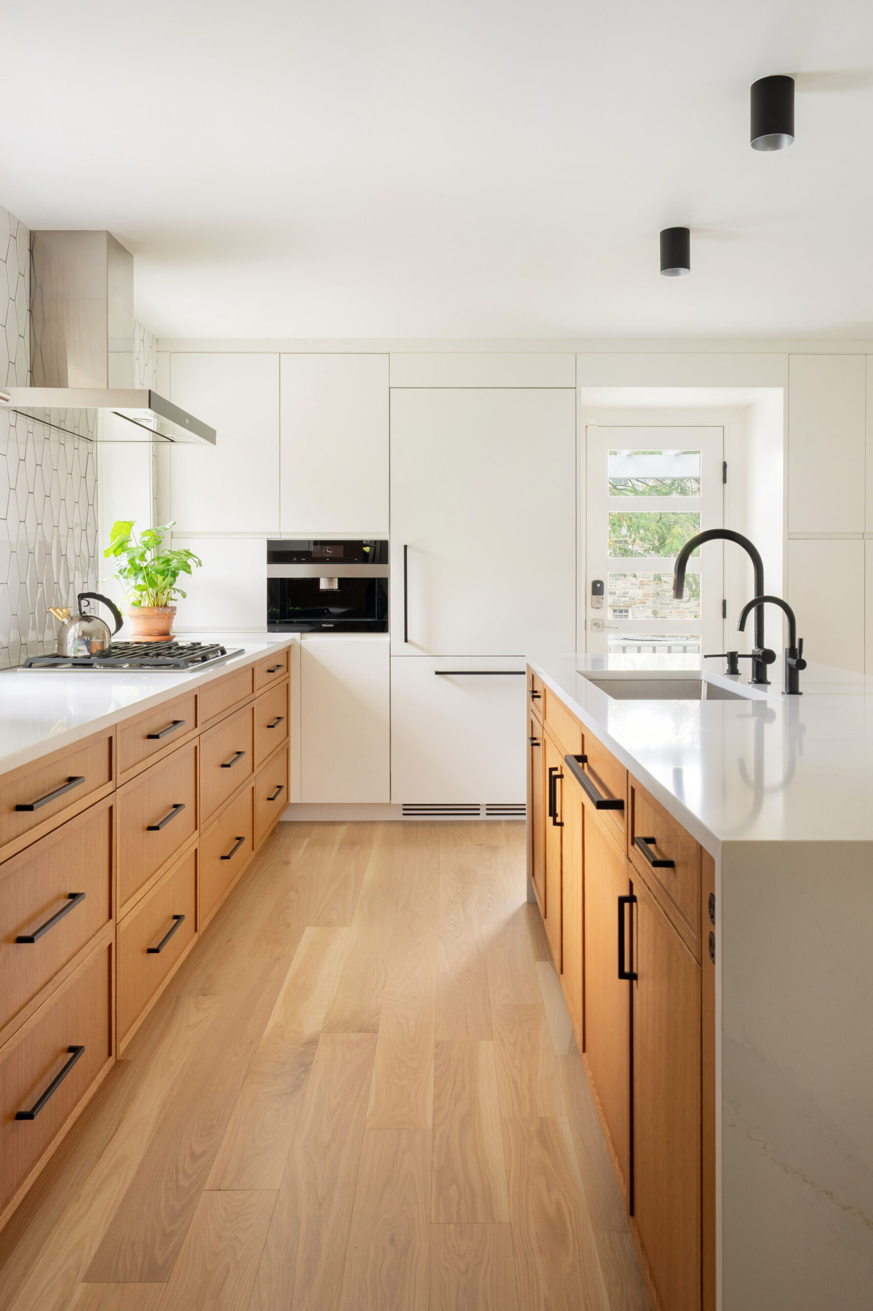 Contemporary kitchen design featuring warm oak cabinetry, matte black hardware, and clean white surfaces with minimalist details.