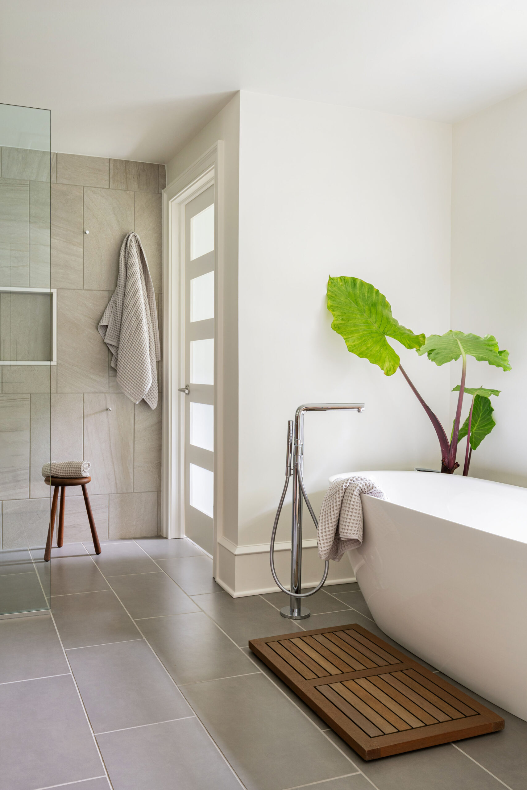 Serene primary bathroom with freestanding soaking tub, walk-in shower, large-format tile, and wood accents.