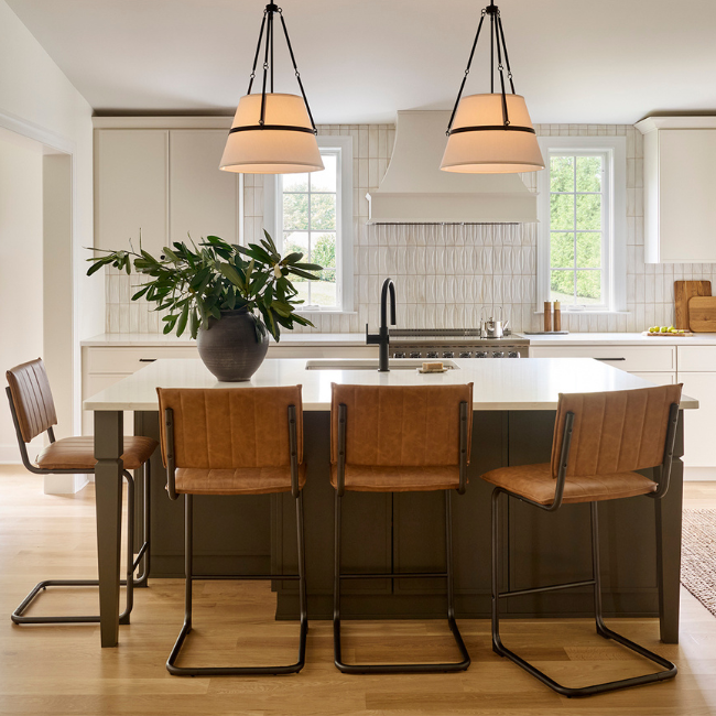 Chesterbrook kitchen with white cabinetry, dark green island, white countertops, dimensional tile backsplash, oversized pendant lights, and brown leather counter stools.