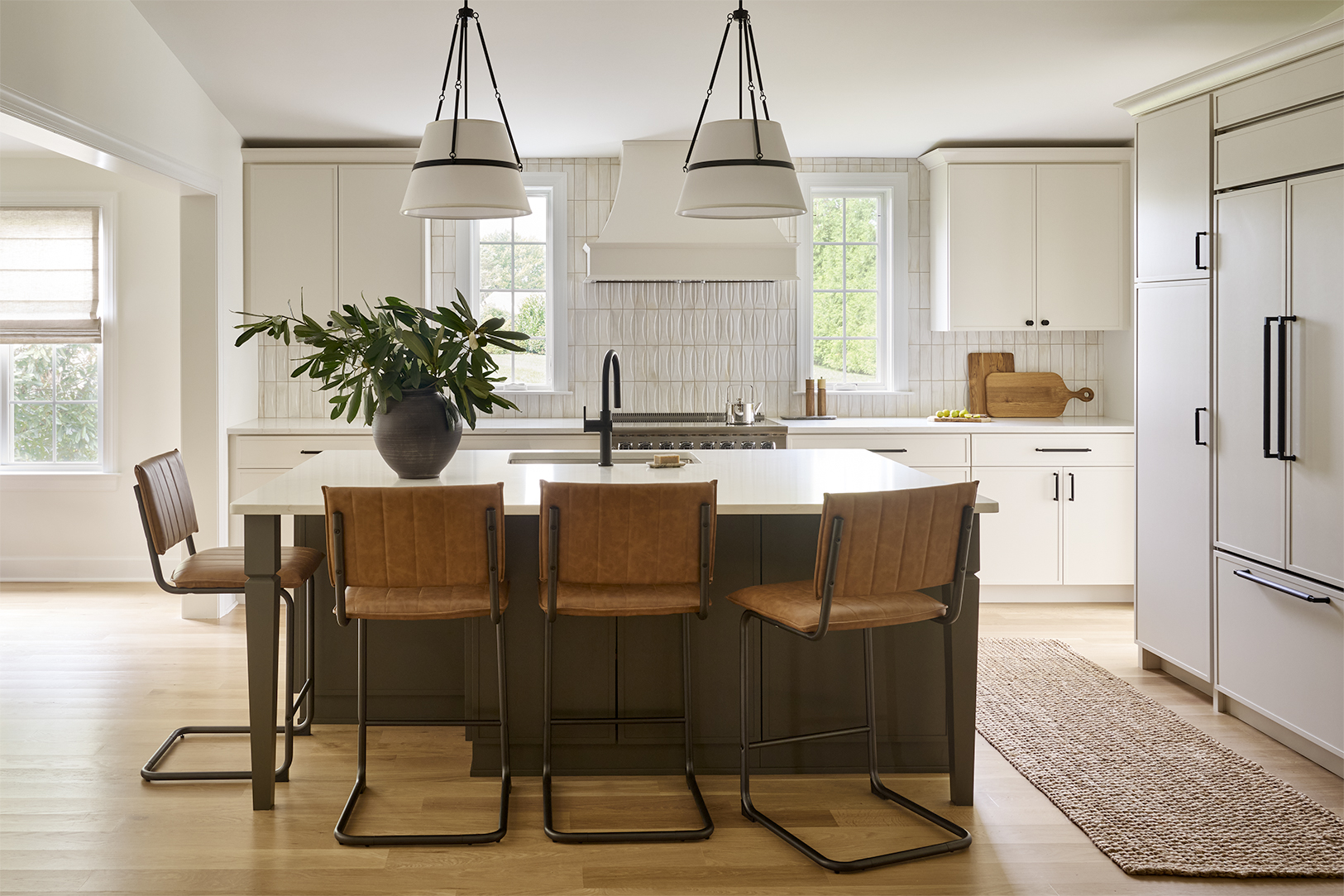 Chesterbrook kitchen with white cabinetry, dark green island, white countertops, dimensional tile backsplash, oversized pendant lights, and brown leather counter stools.