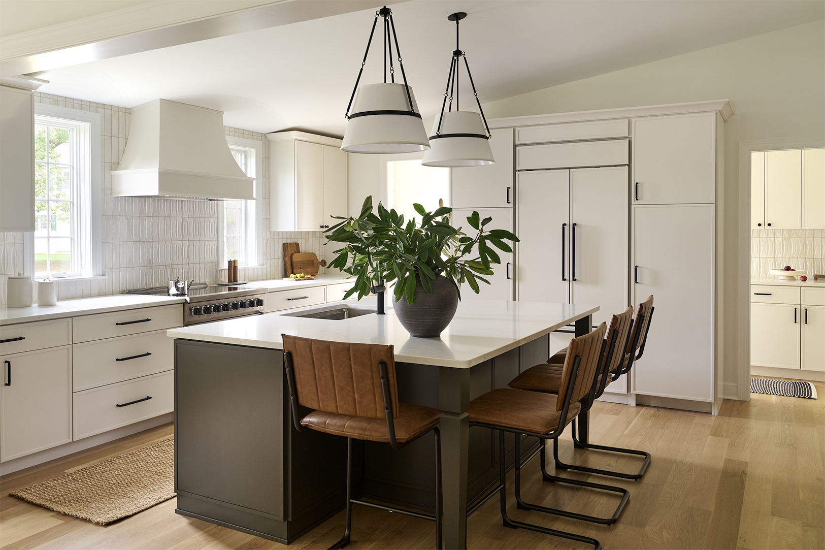 Renovated Chesterbrook kitchen featuring a spacious contrasting island, white cabinetry, black hardware, pendant lighting, and a butler's pantry beyond.