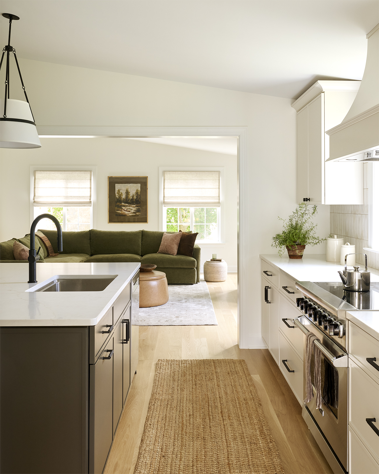 View from the renovated Chesterbrook kitchen into the adjoining living room, featuring a green sectional sofa, wide doorway, white cabinetry, and a contrasting kitchen island.