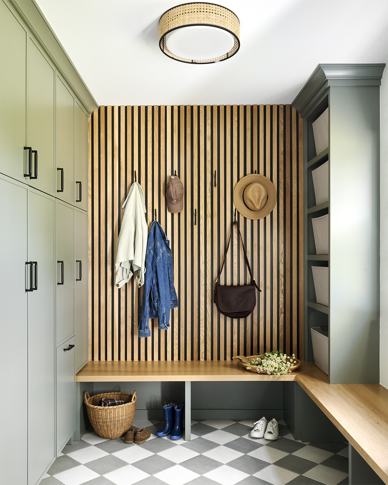 Chesterbrook mudroom featuring sage green built-in cabinetry, vertical natural wood slat accent wall with coat hooks, wraparound wood bench, open shelving, and gray-and-white checkerboard tile flooring.